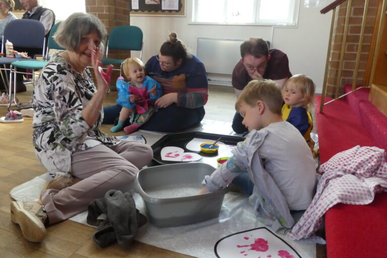 Adults and children sitting on the floor during a worship session in church, with a washing up bowl activity