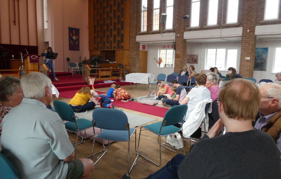 Church worship space with people sat on chairs in horseshoe shape and some people sat on cushions in the centre