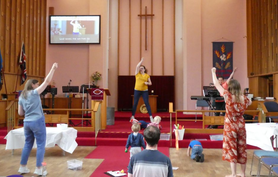 People of all ages worshipping with their hands in the air, in a church space with no chairs.
