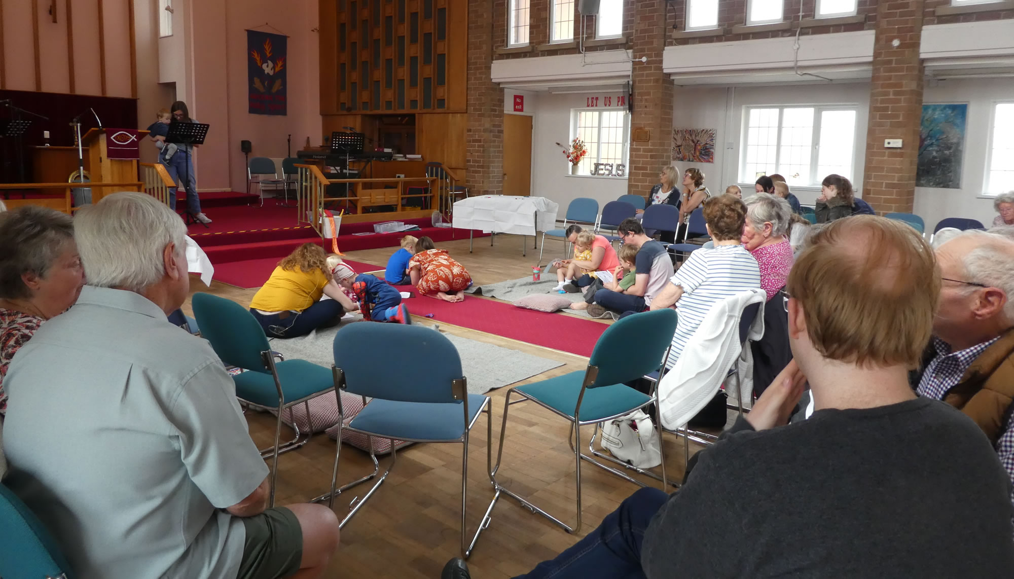 congregation A multi-generational congregation sitting in a church service, with chairs in a horseshoe shape, and an area on the floor with blankets and cushions.