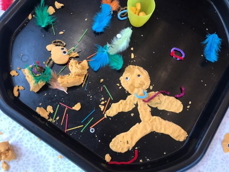 A messy play table with playdough, feathers, pipe cleaners, googly eyes and more
