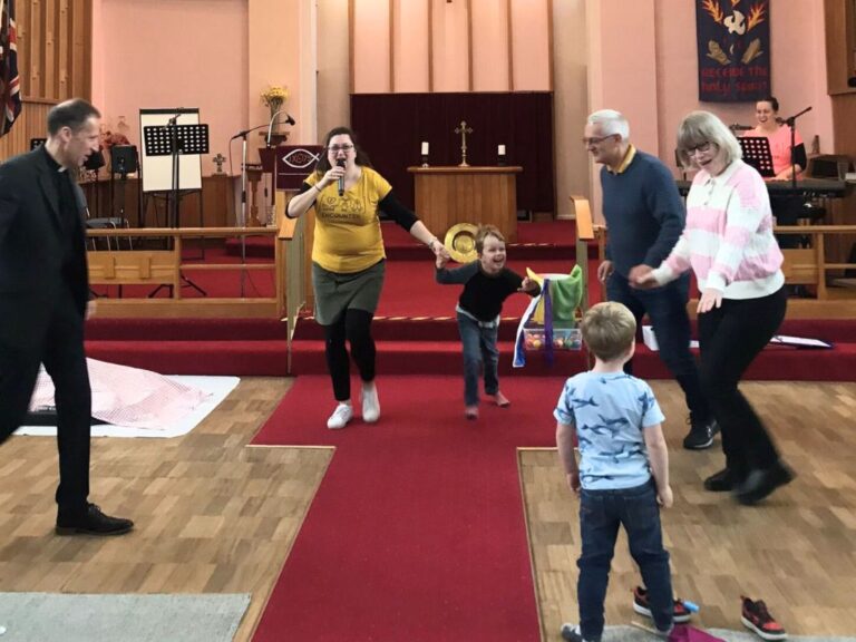 A group of adults and children doing the hokey cokey.