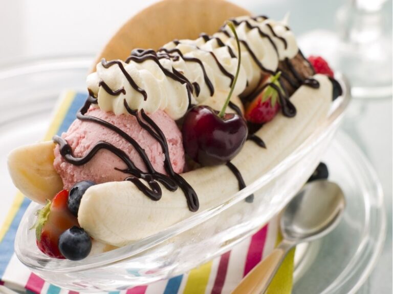 A glass disg containing a banana, fruit, ice cream, whipped cream, chocolate sauce and a wafer.