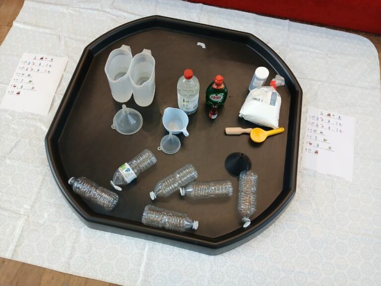 A tuff tray set up with plastic bottles, water, vinergar, bicarbonate of soda and funnels.