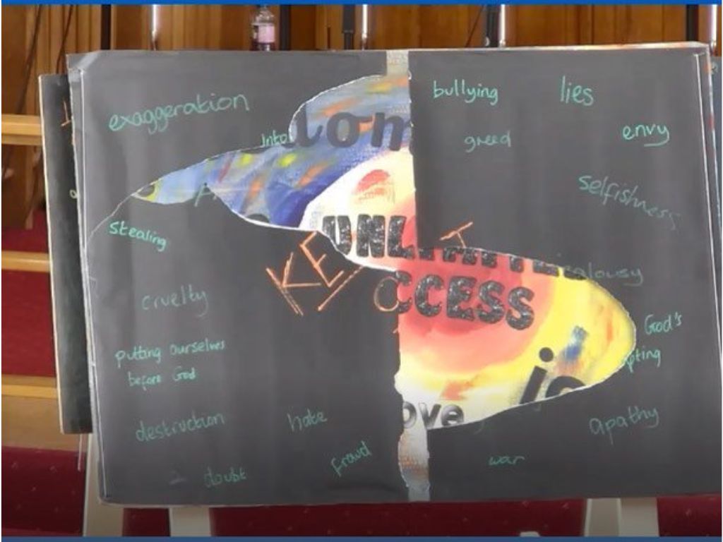 A large black board with the words KEEP OUT in big letters in the middle. Around the edges are different sins, such as pride, greed, lies, bullying, war and hate. Large pieces have been torn away revealing a brightly coloured image behind the black.