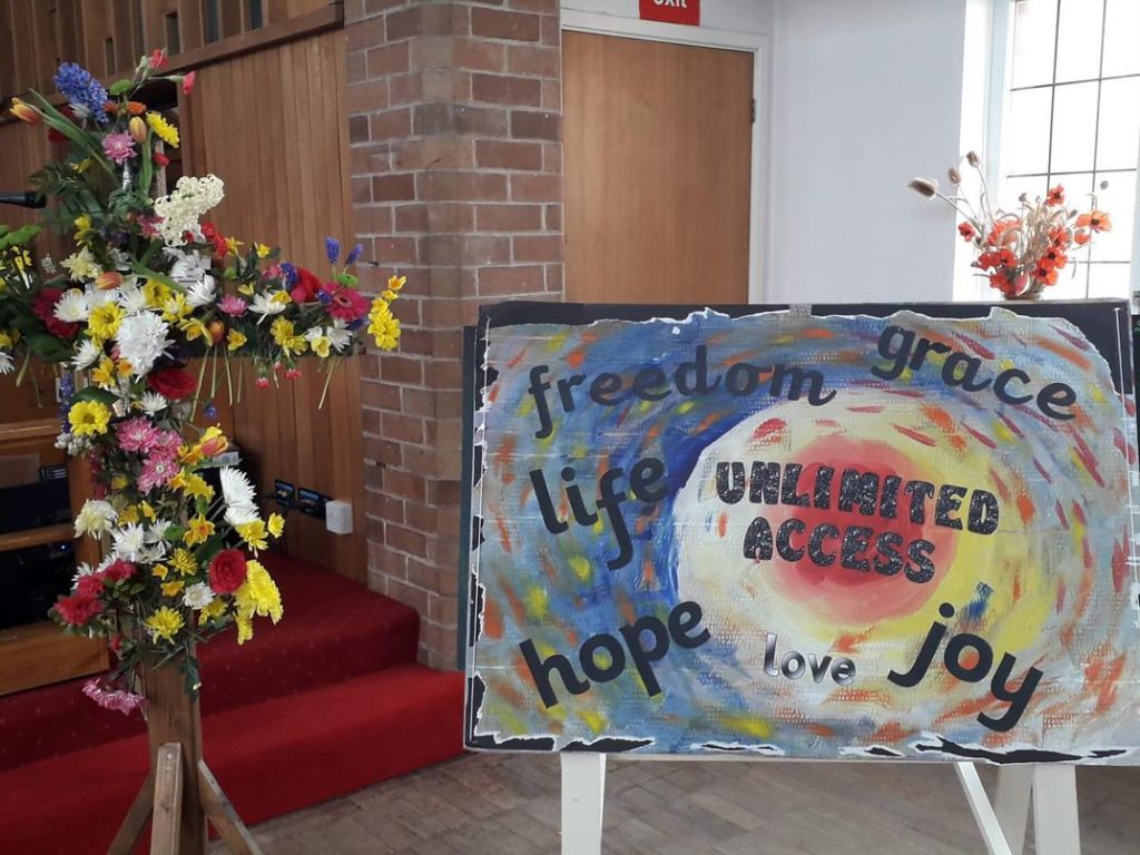 A large brightly coloured board with the words UNLIMITED ACCESS in big letters in the middle. Around the edges are the words freedom, grace, life, hope, love and joy. Large pieces have been torn away revealing a brightly coloured image behind the black. Remnants of the black paper are visible around the edges.