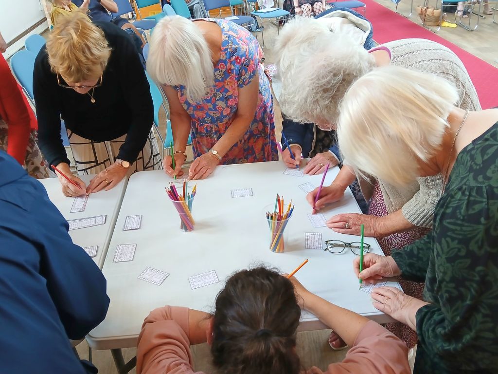 A group of adults are stood around a table colouring.